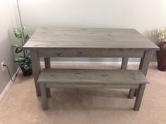 a wooden table and bench sitting in a room next to a potted green plant