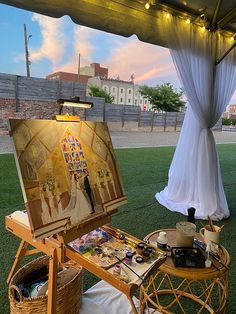 an artist's easel sitting on top of a grass covered field under a tent