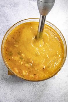 a bowl filled with yellow soup being stirred by a metal blender on top of a table