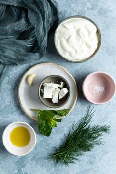 three bowls filled with yogurt and other ingredients on a blue tablecloth next to a green scarf