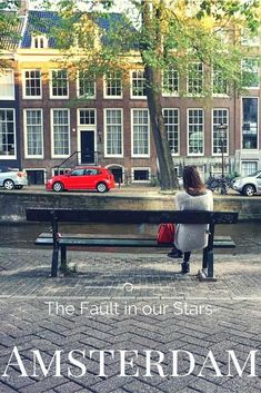 a woman sitting on a bench in front of a red car and some buildings with the words, the fault in four stars amsterdam