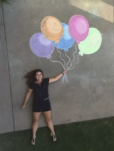 a woman standing in front of a wall with balloons drawn on the sidewalk and chalk