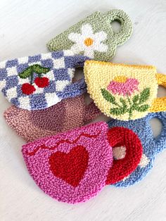 six crocheted tea cups with hearts and flowers on them, all in different colors