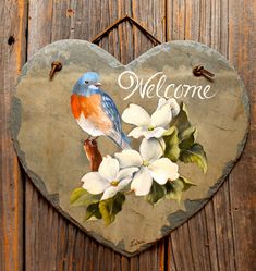 a heart shaped sign with a blue bird and white flowers on it that says welcome