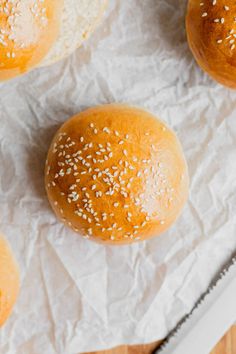 three buns with sesame seeds on them sitting on wax paper