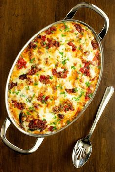 a casserole dish with meat and cheese in it on a wooden table next to a fork