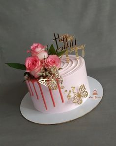 a birthday cake decorated with pink roses and gold butterflies is on a white platter