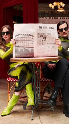 a man and woman sitting at a table with a newspaper in front of their faces