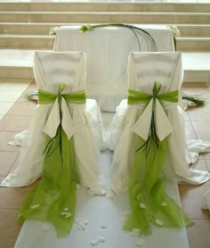 two white chairs with green sashes and bows on the floor in front of some stairs