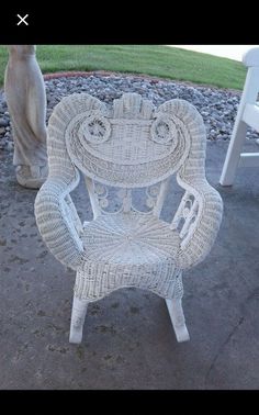 a white wicker chair sitting on top of a cement ground next to a statue