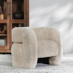 a white chair sitting on top of a rug next to a wooden cabinet and bookcase