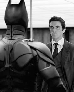 a man in a suit standing next to a batman statue