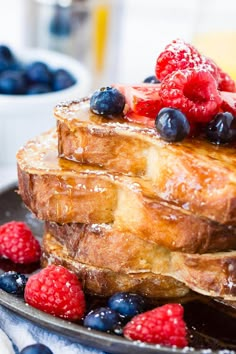 a stack of french toast topped with berries and powdered sugar on a black plate