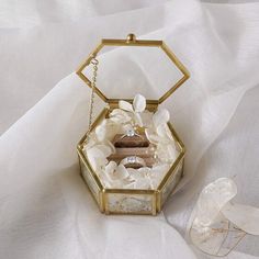 a wedding ring box with white flowers on the inside and gold chain hanging from it