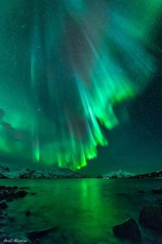 the northern lights shine brightly in the night sky over a body of water and snow covered mountains