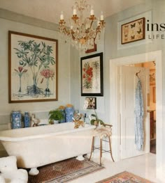 a white bath tub sitting under a chandelier next to a painting on the wall