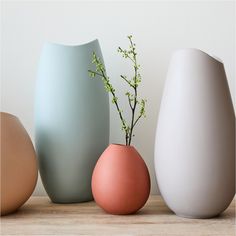 three different colored vases sitting next to each other on a wooden table with flowers in them