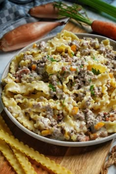 a bowl filled with pasta and meat on top of a wooden cutting board next to carrots