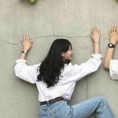 two women sitting against a wall with their hands up