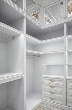 an empty walk in closet with white shelves and drawers