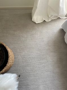 a white bed sitting next to a basket on top of a carpeted bedroom floor