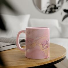 a pink marbled coffee mug sitting on top of a wooden table next to a mirror