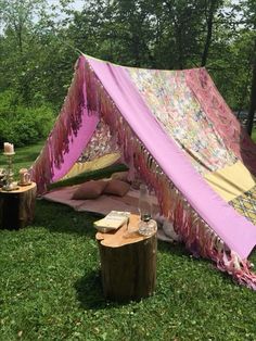 a pink and yellow tent sitting on top of a lush green field next to a tree stump