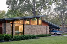 a modern house with large windows and brick walls in the front yard, surrounded by trees