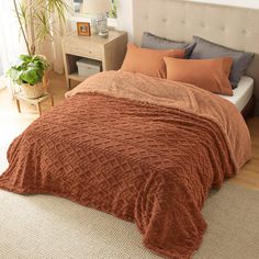 a bed with an orange blanket on top of it next to a night stand and potted plant