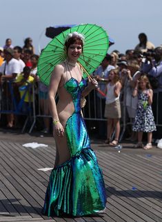 a woman in a green and blue dress with an umbrella standing on a wooden deck