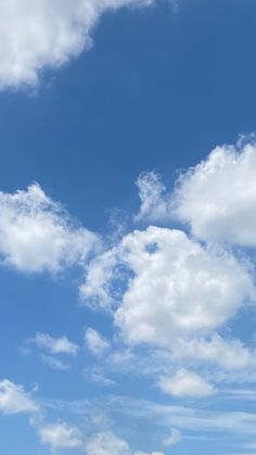 two people standing on the beach flying a kite under a blue sky with white clouds