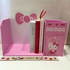 a pink hello kitty bookend with two books in it and a red bow on top