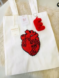 a white tote bag with a red heart on the front and two pom - poms hanging from it