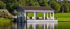 a white gazebo sitting on top of a lake next to a lush green field