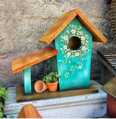 a birdhouse with flowers painted on it and potted plants next to the house