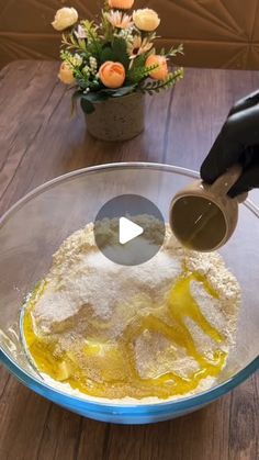 someone is mixing ingredients in a bowl on a wooden table next to a vase with flowers