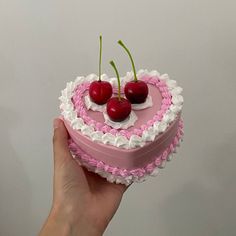 a hand holding a heart shaped cake with cherries on top and white icing