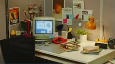 an office desk with a computer monitor, phone and other items on top of it