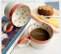 a cup of coffee next to a book and a muffin on a cutting board