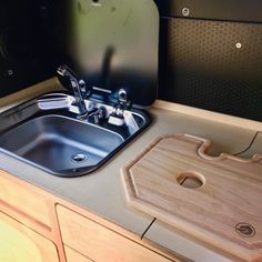 a kitchen sink with a cutting board on the counter top and an oven in the background