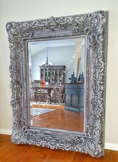 an ornate silver framed mirror sitting on top of a hard wood floor next to a dining room table