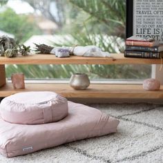 a pink pillow sitting on top of a white rug next to a wooden shelf filled with books