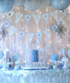 a table topped with lots of blue and white desserts next to a wall covered in snowflakes