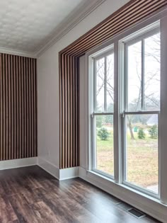 an empty room with wood flooring and striped wallpaper on the walls, along with large windows