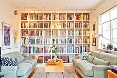 a living room filled with lots of furniture and bookshelves in front of a window