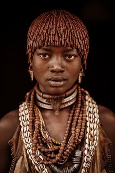 a woman from the african tribe with large beads and necklaces on her head, looking at the camera