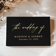 a black and gold wedding guest book on a white table cloth with dried flowers in the background