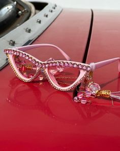 Dramatic, eye catching, and ultra fabulous, these Funnies are truly a MUST HAVE accessory! Surrounded by fun sparkly gold and pink rhinestones, the cat eye lenses are made in a dramatic pink hue. As if these glasses could be any more amazing, the stems have removable hanging crystal tassels at the temple that with eye-catching rhinestone beads. The not-so-subtle gold and pink neck chain can easily be removed. Guaranteed to bring the fabulous disco vibes with you everywhere you go, these out-of-t Gold Cat Eye Party Sunglasses With Glass Lenses, Gold Cat Eye Sunglasses For Party, Gold Glass Cat Eye Sunglasses For Party, Elegant Pink Sunglasses For Party, Elegant Pink Party Sunglasses, Pink Cat Eye Party Sunglasses, Pink Cat Eye Sunglasses For Parties, Party Pink Cat Eye Sunglasses, Elegant Pink Cat Eye Sunglasses For Party