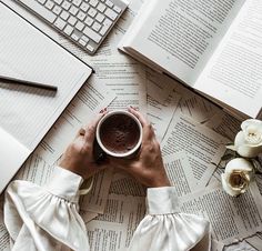 a person sitting at a table with an open book, laptop and cup of coffee