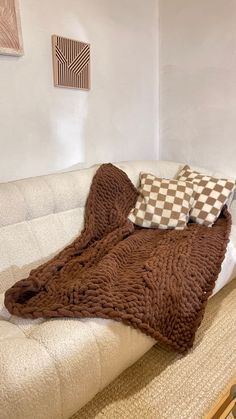 a white couch with two pillows on top of it and a brown blanket over the back